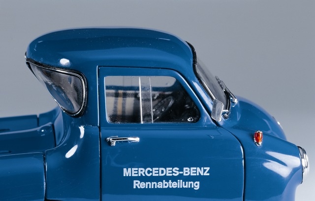 Mercedes Benz Renntransporter (1954) CMC M036 1/18 La cabina destaca en su parte trasera con la original luneta invertida que permitía acomodar el vehículo, sin que la parte delantera del mismo sufriera daños en el transporte.
